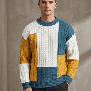 Pode incluir: Uma camisola de manga comprida com gola redonda, apresentando um padrão de malha trançada em blocos de cores amarelo mostarda, branco e azul-petróleo. A peça possui gola, punhos e bainha canelados, com uma construção de malha grossa.