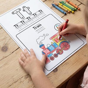May include: A child coloring a train illustration on a white worksheet with the letter "T" and the word "Train" printed on it. Crayons in various colors are scattered on the wooden surface.