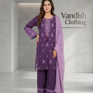 May include: A deep purple three-piece outfit featuring a long-sleeved tunic with intricate white embroidery, matching wide-leg trousers with a patterned hem, and a light lavender sheer dupatta. The text Vandish Clothing is visible on the wall.