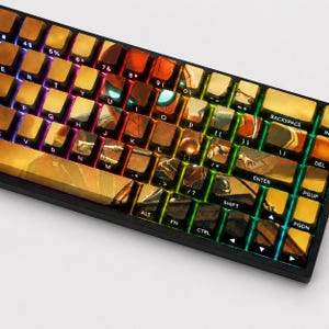 Könnte beinhalten: Eine mechanische Tastatur mit individuellen Tastenkappen, die eine Grafik eines Superhelden in einem rot-goldenen Anzug zeigen. Die Tasten tragen die Standard-QWERTY-Zeichen, einschließlich Buchstaben, Zahlen und Funktionstasten.