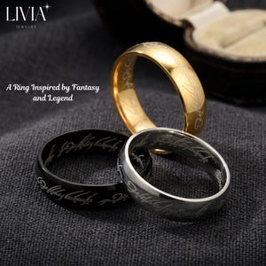 以下が含まれることがあります： ゴールド、ブラック、シルバーの3つの金属製リング。それぞれの外側のバンドには刻印されたスクリプトパターンが施されています。画像左上には「LIVIA JEWELRY」および「A Ring Inspired by Fantasy and Legend」というテキストが表示されています。