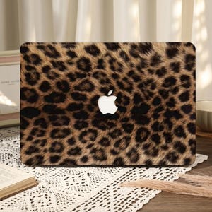 May include: A laptop cover featuring a leopard print design in shades of brown and black. The cover has a white Apple logo in the center. The laptop cover is rectangular and appears to be made of a hard, protective material.