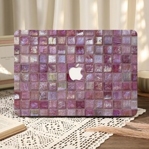 Puede incluir: Una funda para portátil con un diseño de mosaico de azulejos en tonos morados, rosas y blancos. La funda presenta un logotipo de Apple blanco en el centro. El patrón de mosaico está formado por pequeños azulejos cuadrados.