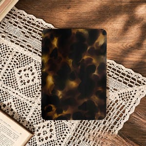 Pode incluir: Uma capa retangular para tablet com um padrão de tartaruga brilhante em tons misturados de castanho escuro, preto e âmbar. A superfície tem um acabamento liso e reflexivo com cantos arredondados, exibindo um design de estampa animal.