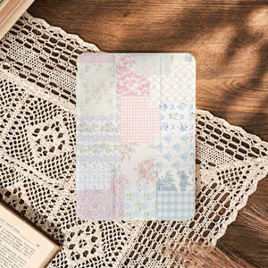 May include: A rectangular tablet case featuring a patchwork design of various floral, gingham, and toile patterns in soft shades of pink, blue, and white. The surface displays a grid-like arrangement of different fabric-inspired prints.