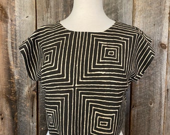 May include: A black and white geometric patterned cropped top with a scalloped hem. The top is on a white mannequin.