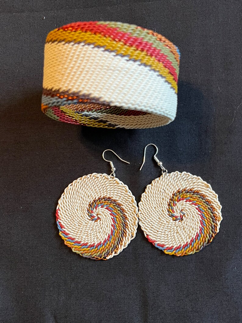 May include: A set of earrings and a bracelet made of woven white cord with colorful stripes. The earrings are circular and have a spiral design. The bracelet is a wide band with a diagonal stripe pattern.