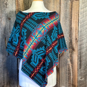 Pode incluir: Um poncho preto e azul-petróleo com um padrão geométrico. O padrão inclui acentos vermelhos, laranja e amarelos.