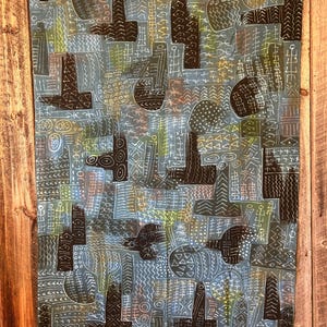 Puede incluir: Un tapiz de pared de tela azul con un patrón geométrico en blanco y negro. El patrón está formado por líneas, círculos y triángulos. La tela es texturizada y tiene un aspecto ligeramente descolorido.