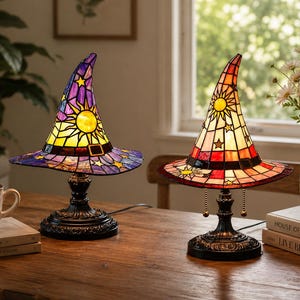 May include: Two stained glass lamps shaped like witch hats. The left lamp features purple and yellow glass with sun and star motifs. The right lamp features red, orange, and yellow glass with sun and star motifs. Both have black metal bases.