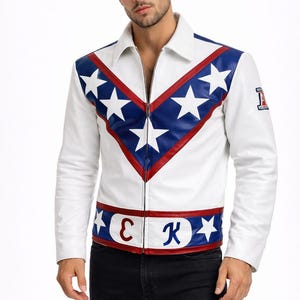 Può includere: Giacca in pelle bianca con un design patriottico con dettagli blu e rossi e stelle bianche. La giacca ha una chiusura con cerniera e una piccola toppa sulla manica. La parte inferiore della giacca ha le lettere "E" e "K".