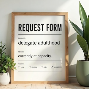 May include: A framed print with the words "REQUEST FORM" at the top. The text below reads "delegate adulthood" and "currently at capacity." The priority options are "LOW," "NORMAL," "HIGH," and "DESPERATE," with "DESPERATE" checked. The frame is light brown.