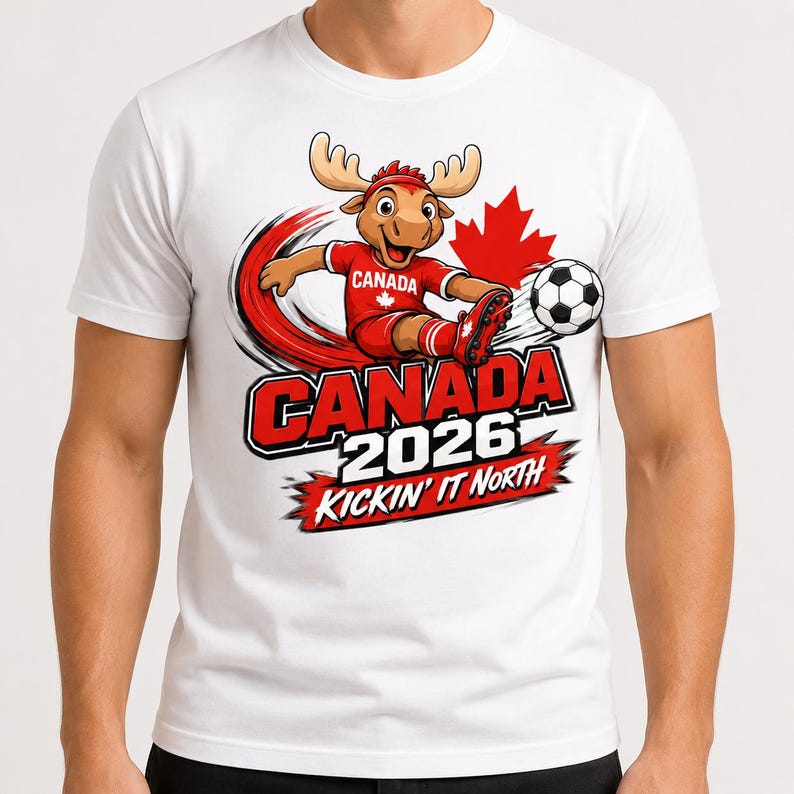 May include: A white t-shirt featuring a cartoon moose wearing a red soccer uniform and kicking a soccer ball. The graphic includes a red maple leaf, the text CANADA 2026, and the phrase KICKIN' IT NORTH in bold red and black lettering.