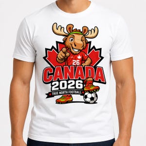 May include: A white t-shirt featuring a cartoon moose mascot wearing a red jersey with the number 26, pointing forward. The design includes a red maple leaf, the text CANADA 2026, and TRUE NORTH FOOTBALL, with the moose standing on a soccer ball.
