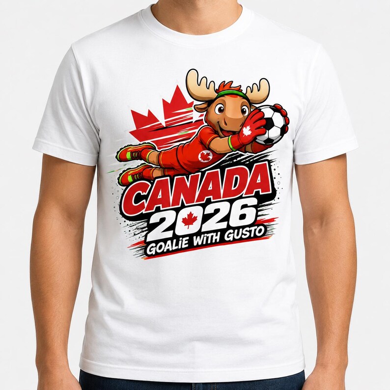May include: A white t-shirt featuring a cartoon moose dressed as a soccer goalie in a red uniform with a maple leaf emblem. The graphic includes a red maple leaf background, a soccer ball, and the text CANADA 2026 GOALIE WITH GUSTO.