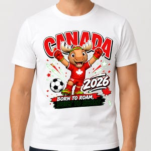 May include: A white t-shirt featuring a cartoon moose mascot wearing a red soccer uniform with a maple leaf, celebrating next to a soccer ball. The graphic includes the text CANADA, 2026, and BORN TO ROAM, BUILT TO SCORE in bold lettering.