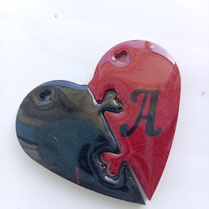 May include: A heart-shaped ornament composed of two interlocking puzzle pieces. The left piece is black with a subtle glitter finish and the letter B, while the right piece is deep red with a glitter finish and the black letter A.