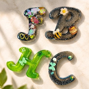 May include: Four resin letters: F, B, H, and C. The F is filled with colorful shells and glitter. The B has a bee, flower, and honey pot. The H is green with shamrocks. The C has shamrocks and glitter.