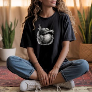 May include: Black t-shirt with a baseball graphic. The design depicts a baseball with a cap, encircled by a smoky effect. The shirt is dark and has a relaxed fit, suitable for casual wear.