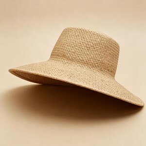 May include: A wide-brimmed sun hat crafted from woven natural tan straw. The hat features a structured, flat-topped crown and a broad, slightly downturned brim, showcasing a consistent, tight basket-weave texture throughout the entire piece.