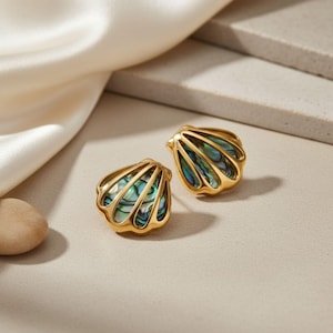 May include: A pair of gold-toned shell-shaped earrings featuring iridescent abalone shell inlays. Each earring has a scalloped metal frame with a polished finish, showcasing the natural green, blue, and purple hues of the shell material.