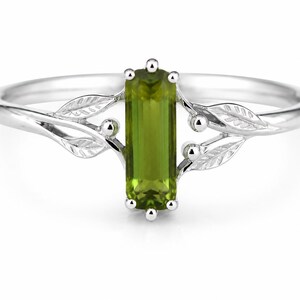 May include: A silver ring featuring a vertical, rectangular, olive-green peridot gemstone set in the centre. The band is designed with delicate, engraved leaf motifs and small spherical accents extending from the sides of the central stone setting.