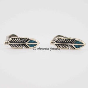May include: A pair of silver feather stud earrings with a turquoise-colored inlay. The earrings have a detailed feather design and are set against a white background. The earrings are a jewelry item.