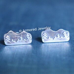 May include: A pair of silver earrings featuring a mountain range design. The earrings are small and delicate, and would make a lovely gift for anyone who enjoys the outdoors.