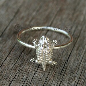 Puede incluir: Un anillo de plata con un diseño detallado de lagarto cornudo. El lagarto está mirando hacia arriba con las patas extendidas.