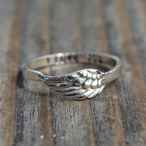 Puede incluir: Un anillo de plata con un dise&ntilde;o de ala de &aacute;ngel. El anillo tiene las palabras "Te amo" inscritas en la banda.