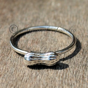 May include: A silver ring with a peanut-shaped design. The ring is simple and elegant, and the peanut is detailed with ridges.