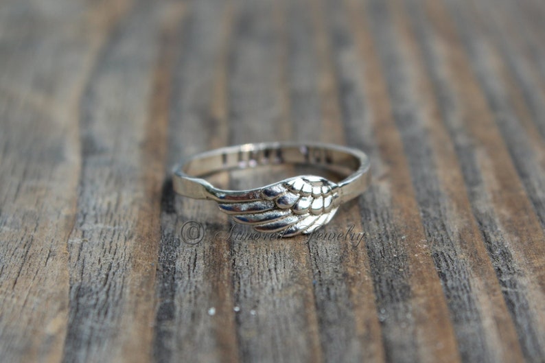 Puede incluir: Un anillo de plata con un dise&ntilde;o de ala de &aacute;ngel. El anillo tiene las palabras "Te amo" inscritas en la banda.
