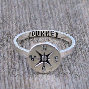 May include: A silver ring with a compass design and the word "JOURNEY" engraved on the band.