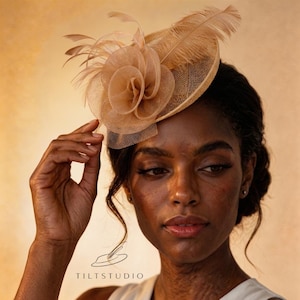 Op de afbeelding: Een beige fascinator met een bloemenontwerp en veermotieven. Het hoofddeksel is gemaakt van een gaasmateriaal en wordt op het hoofd gedragen. De afbeelding bevat ook de tekst "TILTSTUDIO".