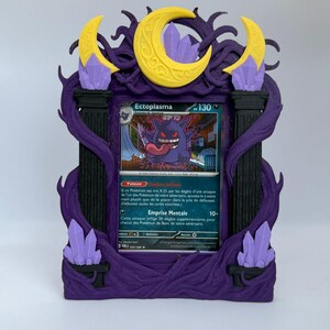 Peut inclure: Un cadre de présentation violet et noir contenant une carte à collectionner Ectoplasma. Le cadre est orné de croissants de lune jaunes, de piliers noirs et de cristaux violet clair, avec des détails en forme de lianes entourant la carte.