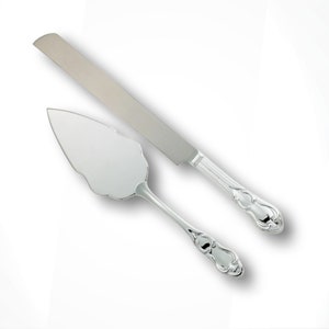 May include: A silver cake knife and server set. The knife has a long, straight blade and a decorative handle. The server has a scalloped edge and a matching handle. Both pieces are made of shiny metal.