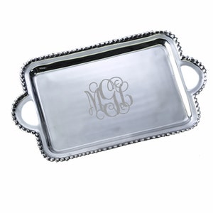 May include: A rectangular silver serving tray with a beaded edge and two handles. The tray features a monogram in the center. The tray is made of a shiny, reflective metal.