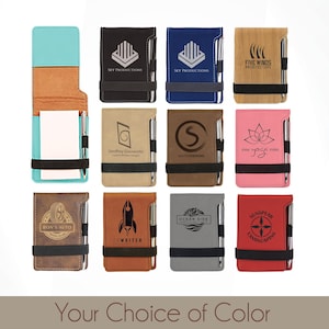 May include: A collection of ten personalized leatherette notebooks with a pen attached. The notebooks are available in a variety of colors, including teal, black, blue, brown, pink, red, and gray. Each notebook features a different design and text, such as "Sky Productions", "Five Winds Architecture", "Geoffrey Glassworks", "Saaten Designs", "Yoga", "Ron's Auto", "The Writer", "Ocean Side", and "SunSpear Landscaping".