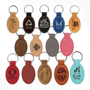 May include: Assortment of oval-shaped leather keychains with various logos and text, including "City Zoo", "Albertson Technology", "Knights", "Mahagiri Suites", "Jackie's Fine Food", "Sky Productions", "Connection Insurance", "Oktoberfest", "North Star Resort", and "Beauty Salon".
