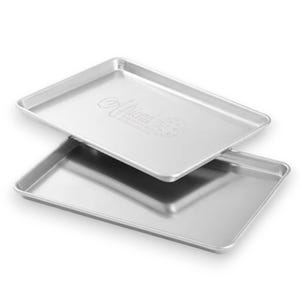 May include: Two silver baking sheets, one stacked on top of the other. The top sheet has the words "All-Clad" embossed on it.