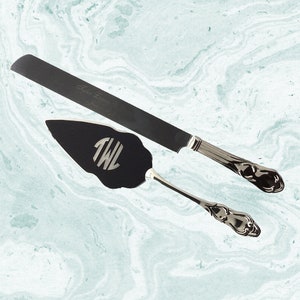 May include: A black cake knife and server set with silver handles. The knife has text engraved on the blade. The server has the initials "TWL" engraved on the blade.