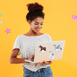 Pode incluir: Uma mulher com um coque no cabelo sorri enquanto olha para um computador port&aacute;til. O laptop tem v&aacute;rios adesivos coloridos, incluindo um unic&oacute;rnio, um cavalo e uma sereia. O fundo &eacute; amarelo brilhante.