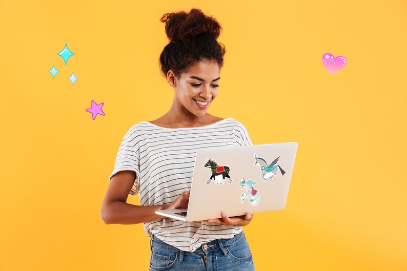 Pode incluir: Uma mulher com um coque no cabelo sorri enquanto olha para um computador port&aacute;til. O laptop tem v&aacute;rios adesivos coloridos, incluindo um unic&oacute;rnio, um cavalo e uma sereia. O fundo &eacute; amarelo brilhante.