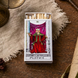 May include: A rectangular matchbox featuring the Justice tarot card illustration on the front, depicting a crowned figure in a red robe holding a sword and scales. The box is partially open, revealing a row of wooden matches with white tips inside.