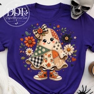 Może przedstawiać: Fioletowy t-shirt z centralną grafiką przedstawiającą postać ducha wykonaną z różnych wzorzystych kawałków materiału, w tym w kratę i kwiaty. Duch ma na sobie dużą kokardę w kratę i pomarańczowe trampki, otoczony kolorowymi kwiatami i gwiazdkami.