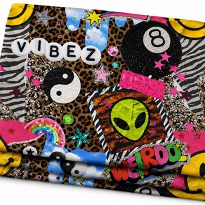 May include: A rectangular fabric piece featuring a collage of leopard and zebra prints, a black eight ball, a yin-yang symbol, a green alien face, yellow smiley faces, and a rainbow. The text VIBEZ and WEIRDO are printed on the surface.