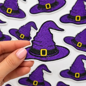 May include: A purple witch hat embroidered patch featuring a black band and a yellow buckle. The patch has a white border and is shown in a repeating pattern with one patch held in the foreground, displaying detailed stitching and texture.