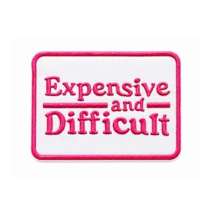 Peut inclure: Un écusson brodé rectangulaire avec un fond blanc et une bordure épaisse rose vif. L'écusson présente le texte brodé en rose vif "Expensive and Difficult" disposé sur trois lignes avec des lignes horizontales séparant les mots.