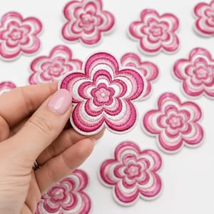 May include: A collection of flower-shaped embroidered patches featuring concentric rings of pink, magenta, and white thread. Each patch has five rounded petals with a dense, textured stitch pattern radiating from the center to the outer edge.