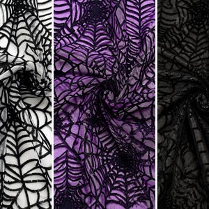 May include: A collection of three fabric swatches featuring a repeating spider web pattern. The first swatch is white with black webs, the second is purple with black webs, and the third is black with black webs, all showing a textured finish.